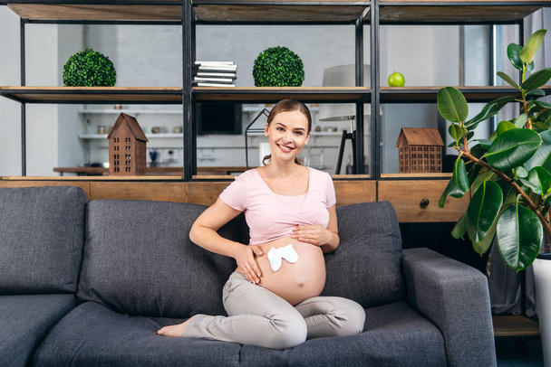 Kaunis raskaana oleva nainen söpö vauva sukat sohvalla kotona
 - Valokuva, kuva