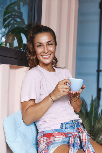 Stay home, cup of coffee and chill. Vertical of dreamy, relaxed smiling girl drinking tea at balcony, staying inside to protect virus spread, self-quarantine covid19 lockdown, relaxing on isolation - Photo, Image
