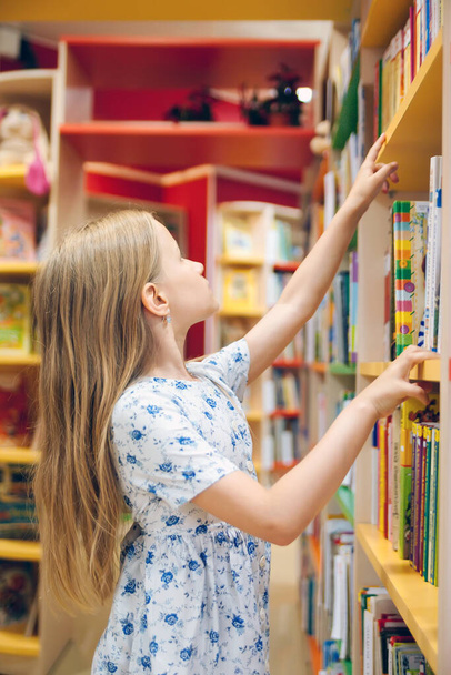  pretty school girl in library choosing books.  - Foto, imagen