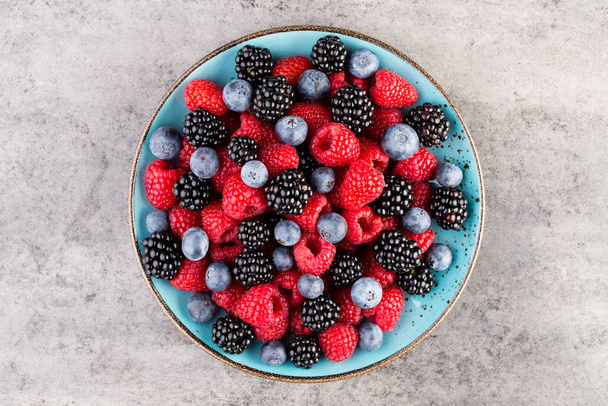 Fresh berries in a plate on a  wooden background. Flat lay, top view, copy space. - Photo, Image