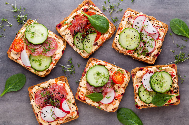 Sandwiches with cream cheese, vegetables and salami. Sandwiches with cucumber, radish, tomatoes, salami on a gray background, top view. Flat lay. - Foto, afbeelding