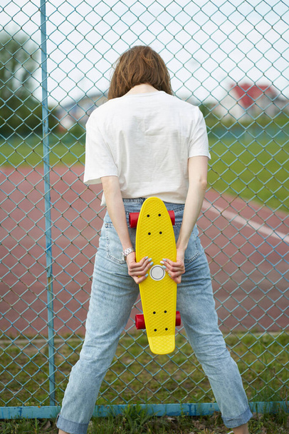 Pelirroja chica blanca con monopatín cerca de valla de pie hacia atrás
 - Foto, imagen