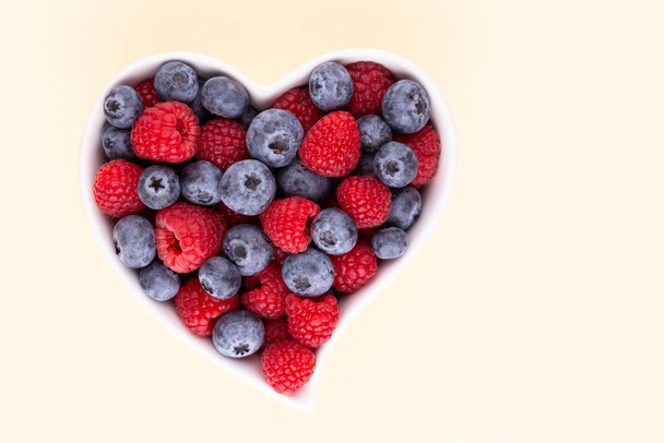 Blueberry and raspberries, fruit in a heart shaped dish on a porcelain bowl pastel background - Foto, Imagen