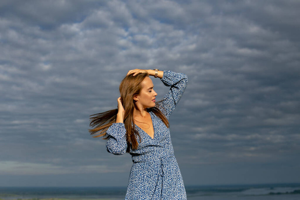štíhlá mladá brunetka s chvějícími se vlasy ve větru stojí proti zamračené obloze - Fotografie, Obrázek