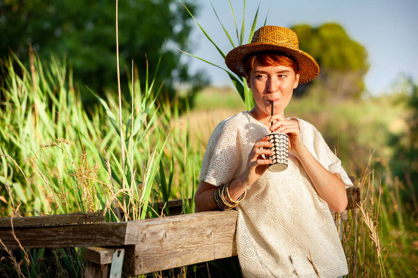 WOMAN WITH STRAW HAT DRINKING FROM STRAW IN THE COUNTRYSID - Photo, Image