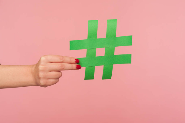 Blog marketing, social media trends. Closeup of female hand holding green hashtag sign, sharing tagged message, famous internet post, promoting web content and viral ideas. indoor studio shot isolated - Foto, Imagem