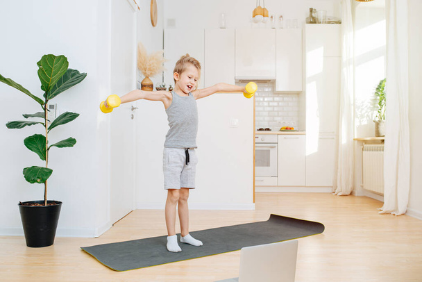  Morning online workout in the kitchen, the boy picks up dumbbells and smiles - Foto, imagen