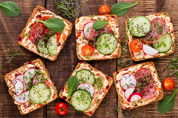 Sandwiches with cream cheese, vegetables and salami. Sandwiches with cucumber, radish, tomatoes, salami on a gray background, top view. Flat lay. - Foto, Bild