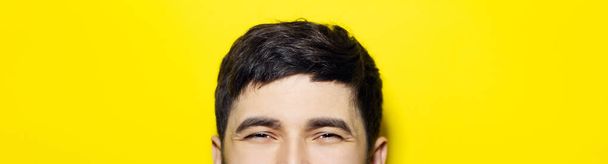 Close-up of smiling eyes of asian guy, panoramic portrait on yellow background. - Foto, Imagen
