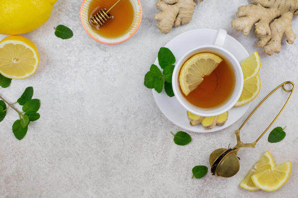 Ginger tea infusion in white cup with lemon slice, mint, honey. Hot healthy beverage on white background. Immune defence, vitamin c. Still life health care concept. Top view. Copy space. - Фото, зображення