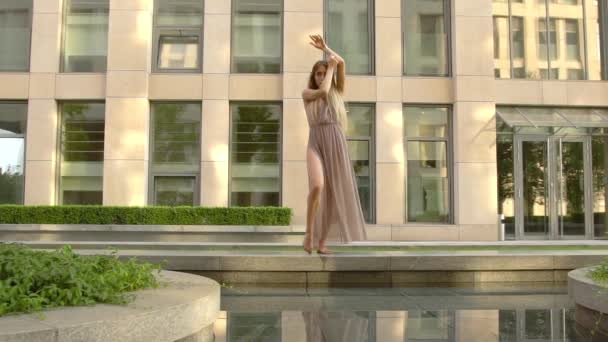 Beautiful young girl dancing on the street of a modern city and is reflected in the water. Slow motion - Filmati, video