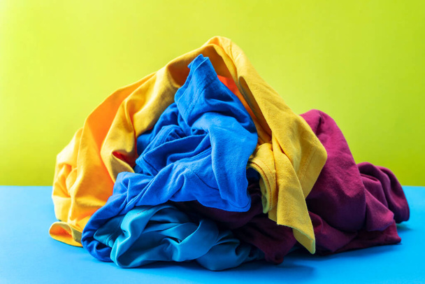 青いテーブルの上に汚れた洗濯服の山黄色の背景 - 写真・画像
