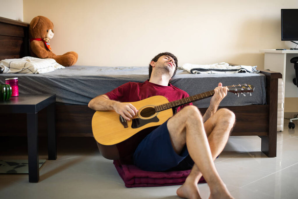 A férfi gitározik a hálószobájában, és otthon gyakorolja a társadalmi távolságot. - Fotó, kép