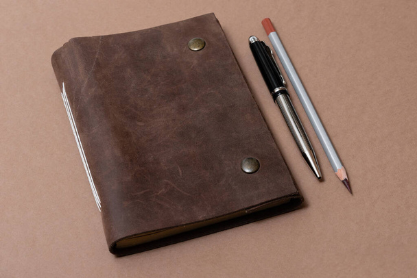 Винтажная кожаная тетрадь и карандаш на коричневом фоне
 - Фото, изображение
