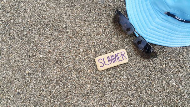 青い帽子、サングラス、そして夏という木。海の砂の上の組成。夏の気分。旅行代理店のためのビーチ写真。スペースのテキスト. - 写真・画像