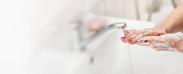 Young woman washing her hands under water tap faucet with soap. Wide banner space for text left side. Personal hygiene concept - coronavirus covid-19 outbreak prevention - Valokuva, kuva