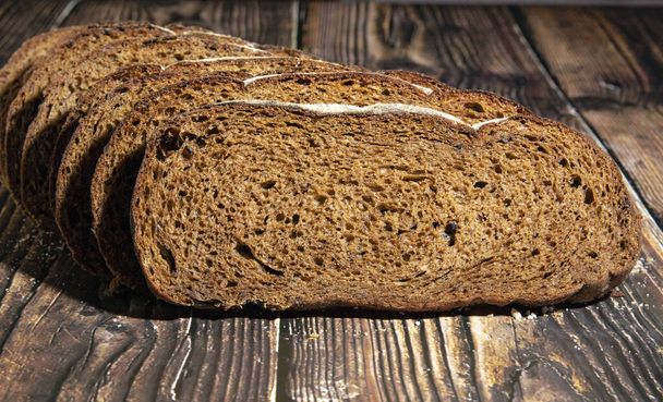 Нарезанный ржаной хлеб на доске. Целое зерно ржаного хлеба на темном фоне. Крупный план
 - Фото, изображение