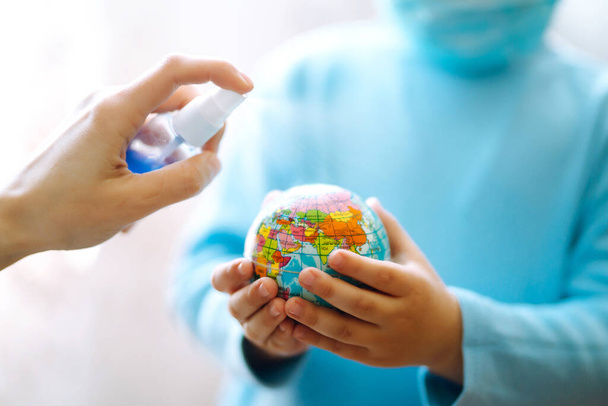 Planeetsterilisatie. Kind in beschermende steriele medische masker met een wereldbol. Red de planeet. Het concept om de verspreiding van het epidemische coronavirus te voorkomen. - Foto, afbeelding