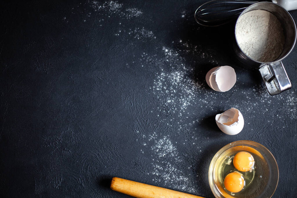Cooking process.Flour, Eggs, Yolk, Shell,whisk,rolling pin.Flour scattered on a black concrete background. - Foto, imagen