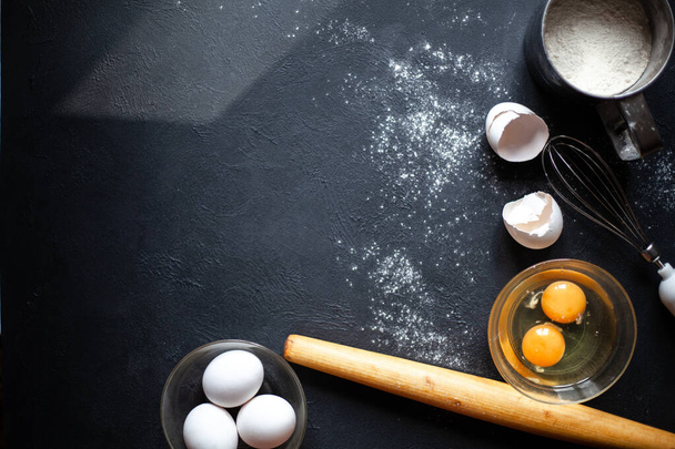 Cooking process.Flour, Eggs, Yolk, Shell,whisk,rolling pin.Flour scattered on a black concrete background. - Photo, Image