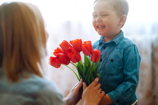 Little son congratulates mother and gives a bouquet of flowers tulips. Happy mother's day. Family holiday and togetherness. - Фото, изображение