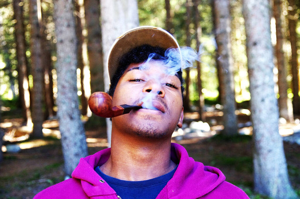 szczęśliwy młody człowiek pali z przyjemnością tytoń w rurze pośród słodkich wirów i chmur dymu - Zdjęcie, obraz