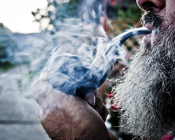 幸せな老人は甘い渦巻きと煙の雲の間で喜びと彼のパイプの中でタバコを吸う - 写真・画像