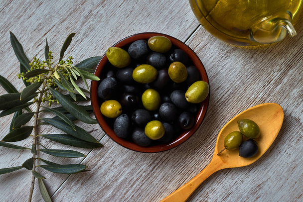 Bowl with green olives, wooden spoon, olive branch and oil - Foto, Bild