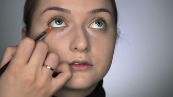 Meikki taiteilija tekee ammatillinen meikki nuori nainen kauneushoitola. Make up Taiteilija soveltaa peitevoide silmien alueella - Materiaali, video