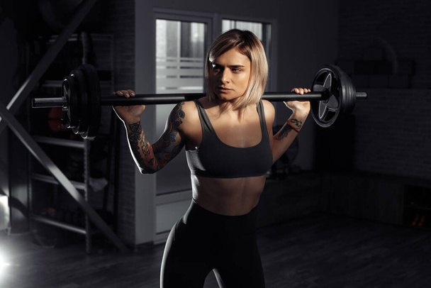 Athletic young blonde woman doing heavy barbell exercise in fitness class. - Foto, Bild