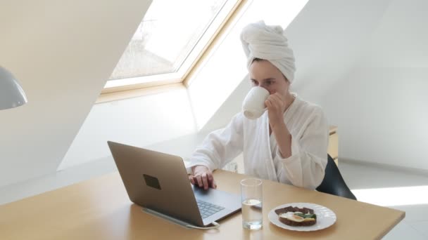 白いバスローブを着たフリーランスの女性頭にタオル。家の隔離の概念を - 映像、動画
