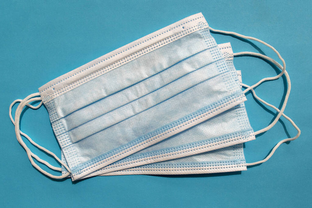 Surgical disposable face masks on blue background. Top view. Medical blue masks. Medical respiratory bandages as preventive measure against viruses. PPE equipment  - Photo, image