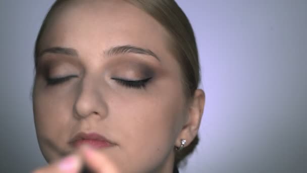 Close up de maquiador fazendo maquiagem profissional para a jovem no estúdio de beleza. Maquiagem Artista desenha flechas sobre o olho, delineador - Filmagem, Vídeo