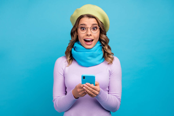 Portrait of astonished excited crazy girl use smartphone impressed social network notification scream wow omg wear trendy violet jumper green headwear isolated over blue color background - Foto, Bild