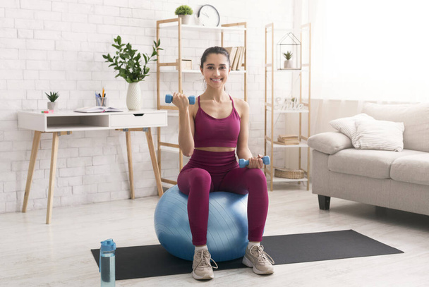 Mujer joven haciendo ejercicios de cardio con pesas y pelota de fitness en casa
 - Foto, imagen