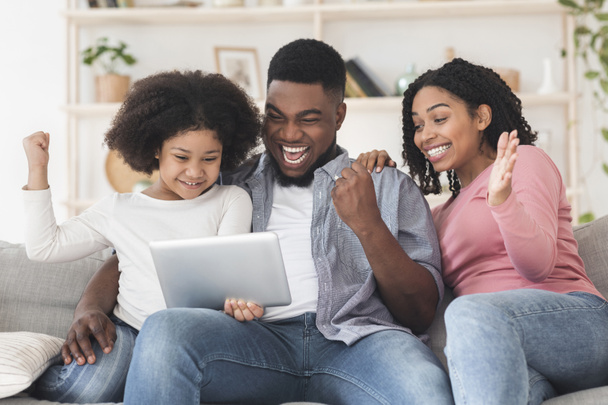Joyful black family celebrating success with digital tablet at home - Fotó, kép