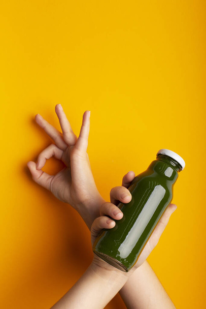 Kobieta trzyma butelkę z zielonym detox smoothie nad żółtym - Zdjęcie, obraz