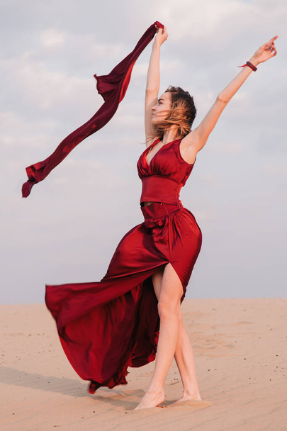 girl in the desert at sunset in a red dress developing in the wind - Foto, Imagem
