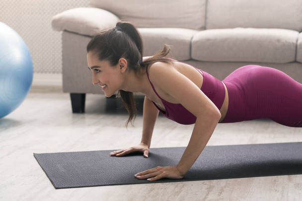 Stay home, stay fit. Latin woman doing push ups in living room - Photo, Image
