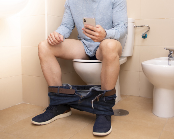 adult man using smartphone while sitting on toilet bowl at home, technology and lifestyle concept - Foto, afbeelding
