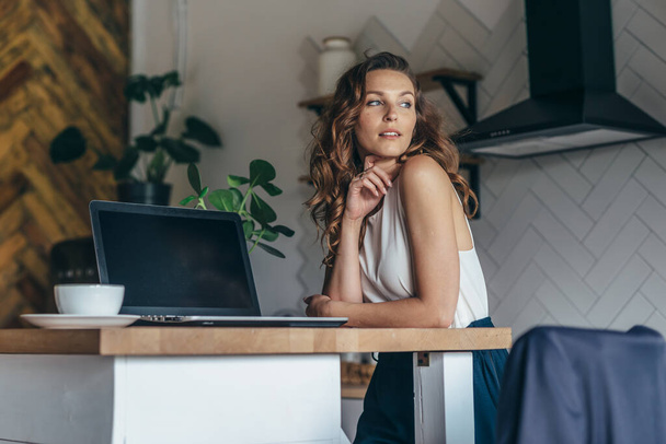 Jeune femme travaillant sur un ordinateur portable et buvant du café tout en étant assis à la maison
 - Photo, image