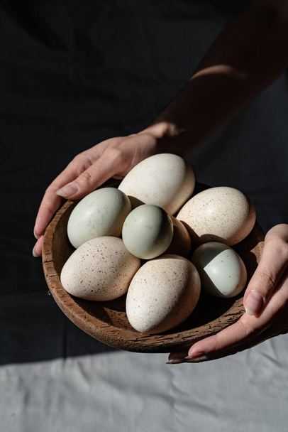 Araucana eggs and goose eggs on a wooden plate in female hands - Fotoğraf, Görsel