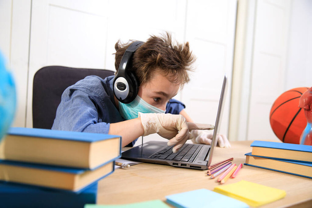 Online onderwijs op afstand. schooljongen met medisch masker die thuis studeert, coronavirus quarantaine - Foto, afbeelding