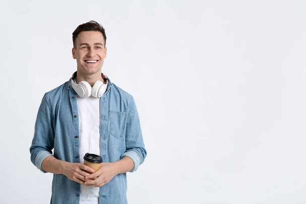 Kerel met koptelefoon glimlachend en houdt koffie - Foto, afbeelding