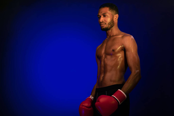 Africký Američan v boxerských rukavicích stojící nad modrým pozadím - Fotografie, Obrázek