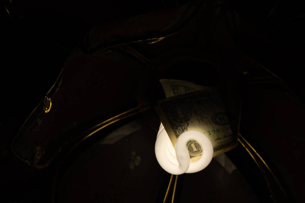 Energiesparlampe mit einem amerikanischen Dollar in einem alten Kronleuchter an der Decke in einem dunklen Raum - Foto, Bild