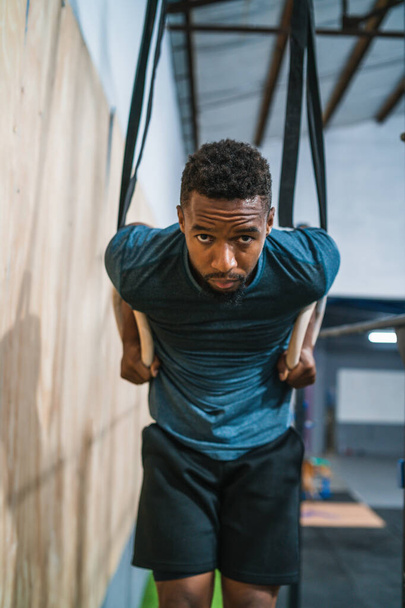 Portrait of young athletic man working out his muscles on rings at the gym. Crossfit, sport and healthy lifestyle concept. - Photo, image