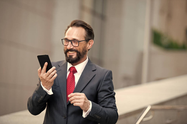 Businessman in glasses using smart phone on office walkway with city building background. Concept of business people using technology. man in suit is searching information on web via mobile phone. - Photo, Image