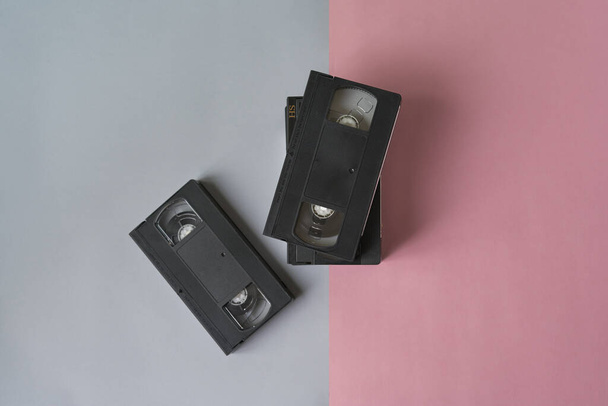 Stapel zwarte vhs videobanden op een roze en grijze achtergrond.Minimalistisch retro concept - Foto, afbeelding