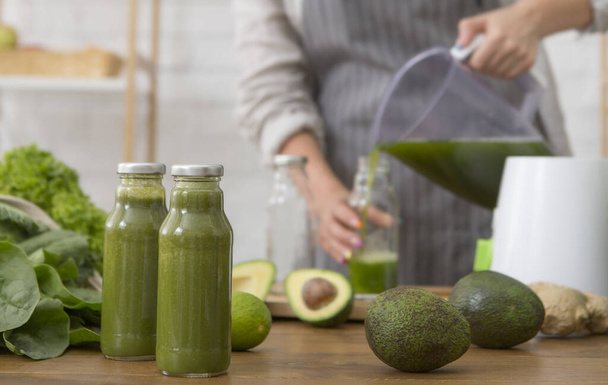 Woman in linen apron pouring green detox smoothie into bottle - Photo, Image